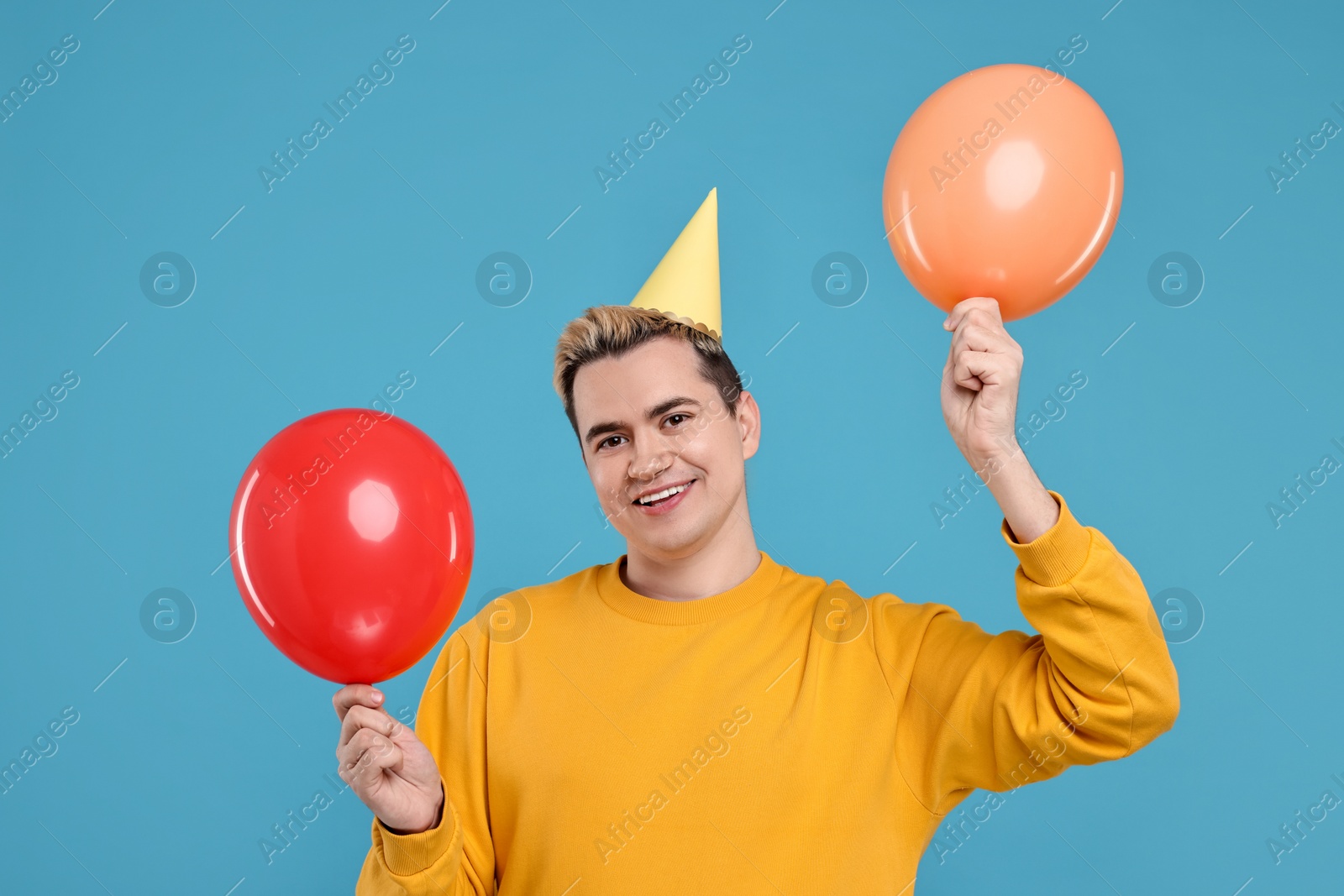 Photo of Young man with party hat and balloons on light blue background
