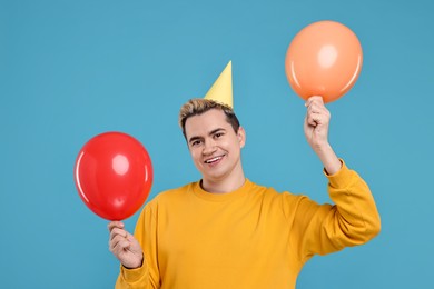 Young man with party hat and balloons on light blue background