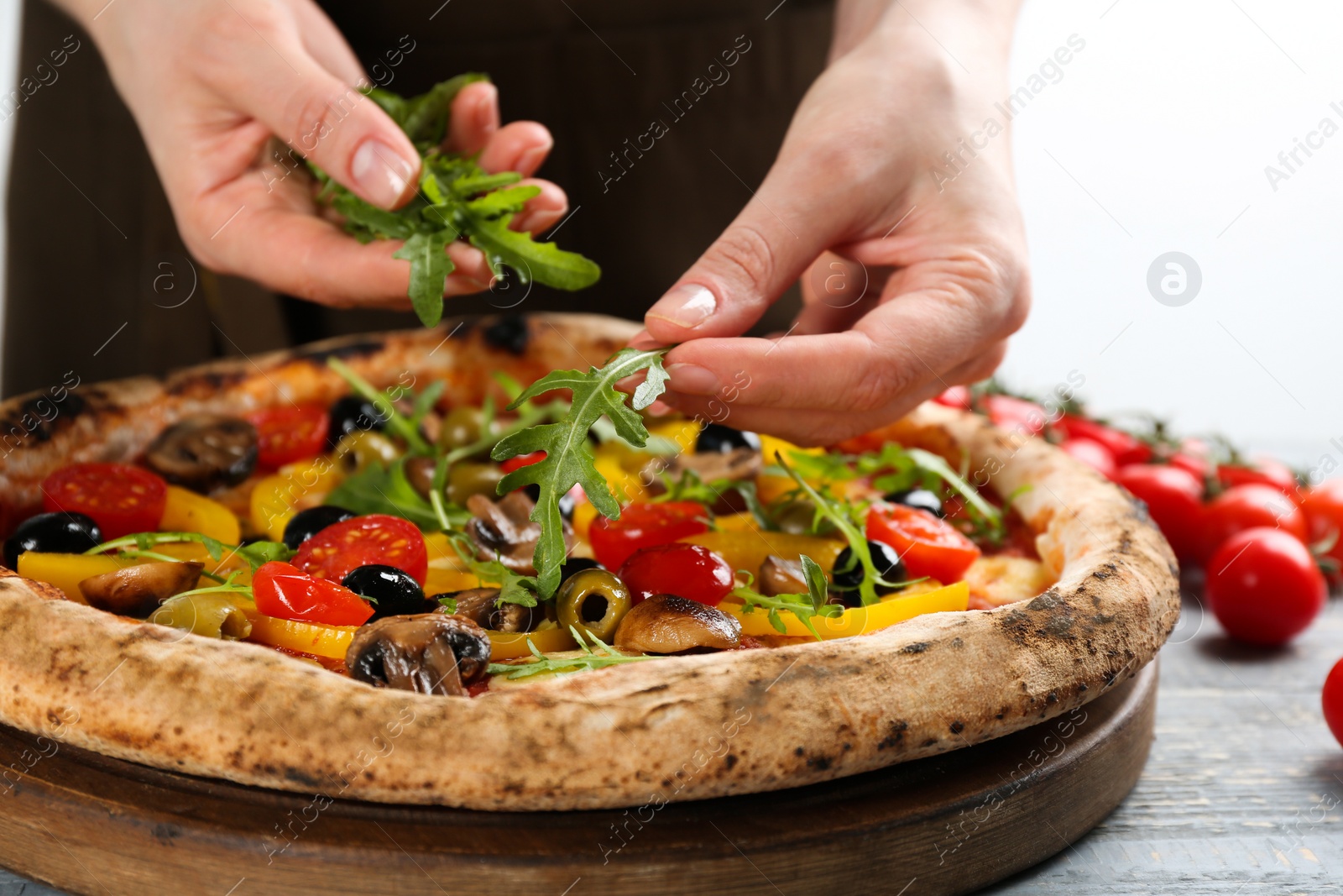 Photo of Woman adding arugula to vegetable pizza at table, closeup