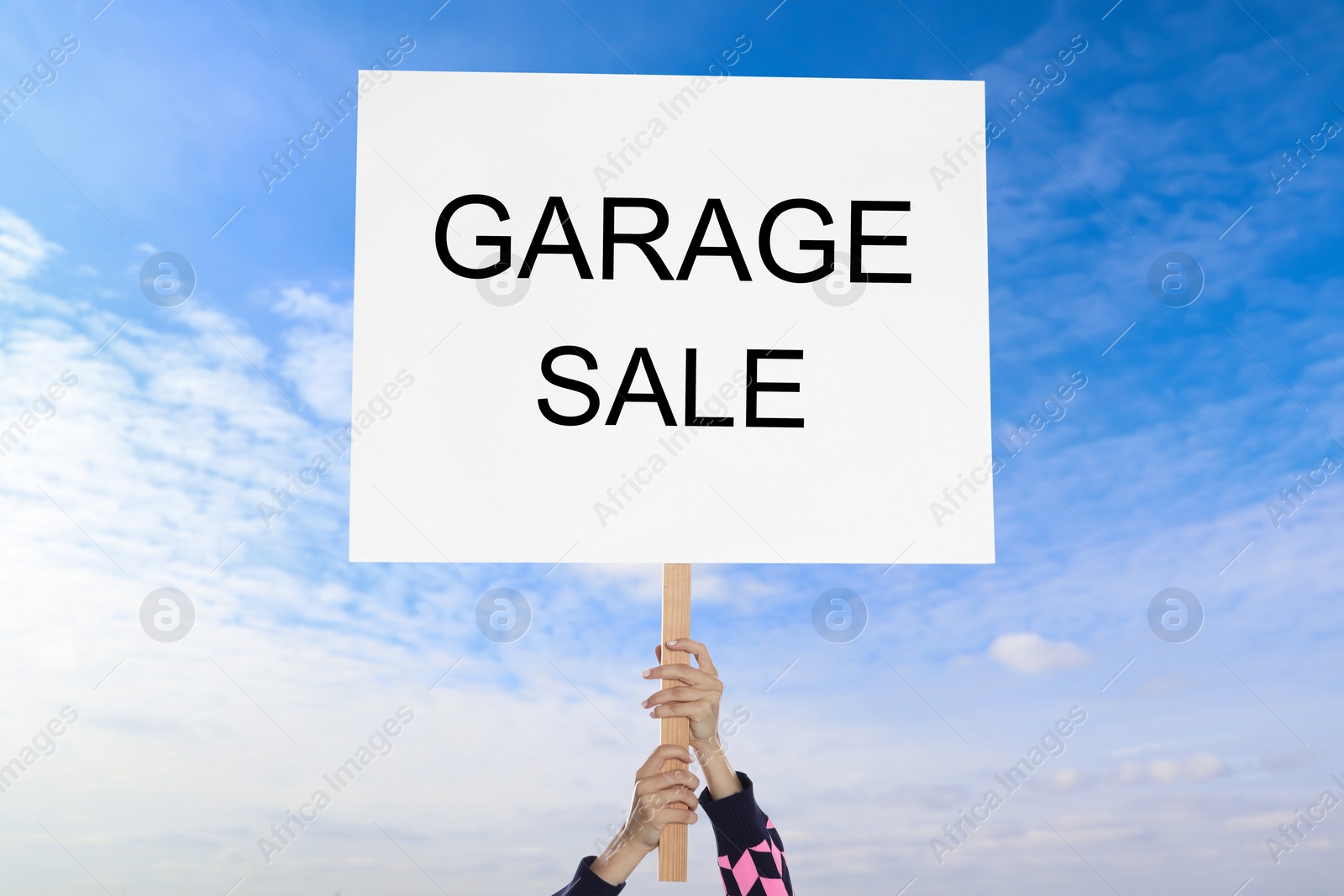 Image of Woman holding sign with text GARAGE SALE against blue sky