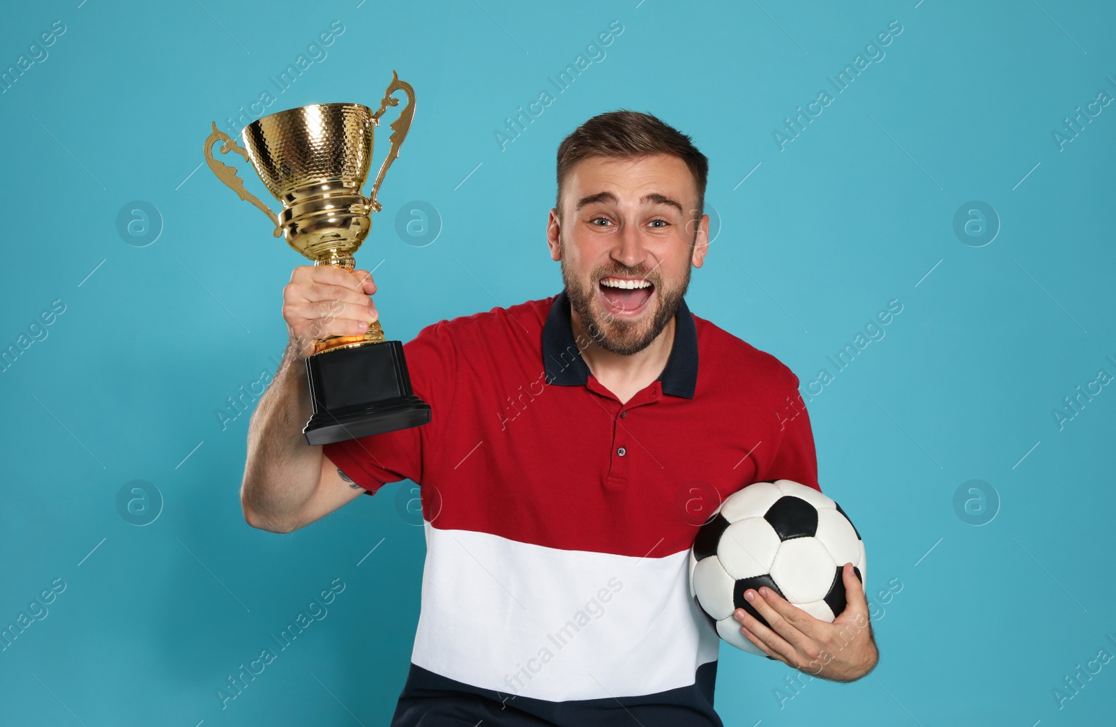 Photo of Portrait of happy young soccer player with gold trophy cup and ball on blue background