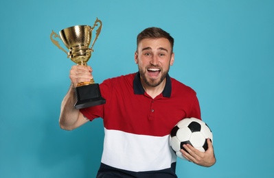 Photo of Portrait of happy young soccer player with gold trophy cup and ball on blue background