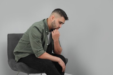 Photo of Sad man sitting near light grey wall. Space for text