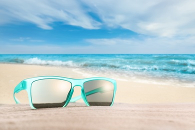 Image of Stylish sunglasses on sandy beach near sea