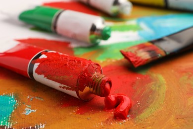 Photo of Tube of red oil paint on canvas with abstract painting, closeup