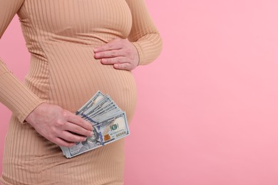 Photo of Surrogate mother. Pregnant woman with dollar banknotes on pink background, closeup. Space for text