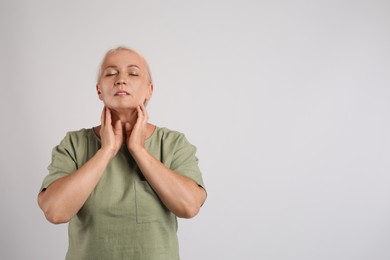 Photo of Mature woman doing thyroid self examination on light grey background, space for text