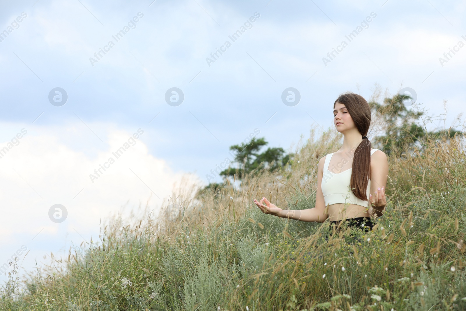 Photo of Teenage girl meditating on hill. Space for text