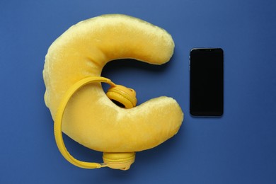 Photo of Yellow travel pillow, smartphone and headphones on blue background, flat lay