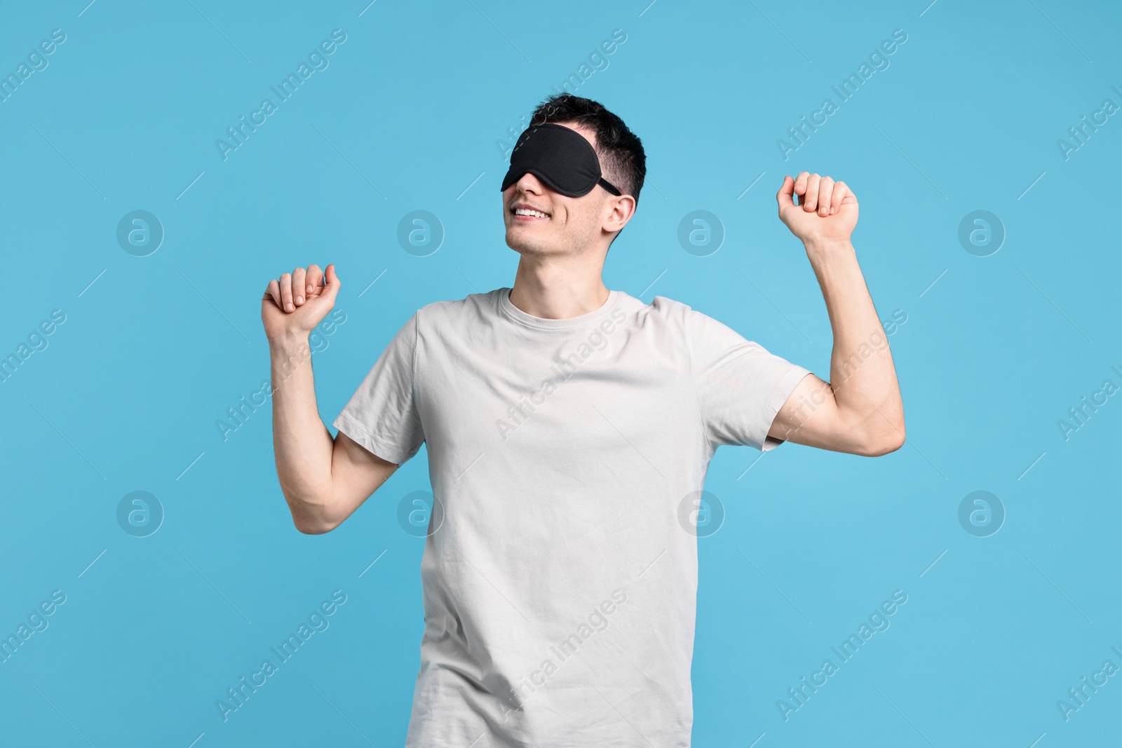 Photo of Happy man in pyjama and sleep mask on light blue background