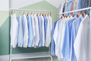 Photo of Racks with clean clothes on hangers after dry-cleaning indoors