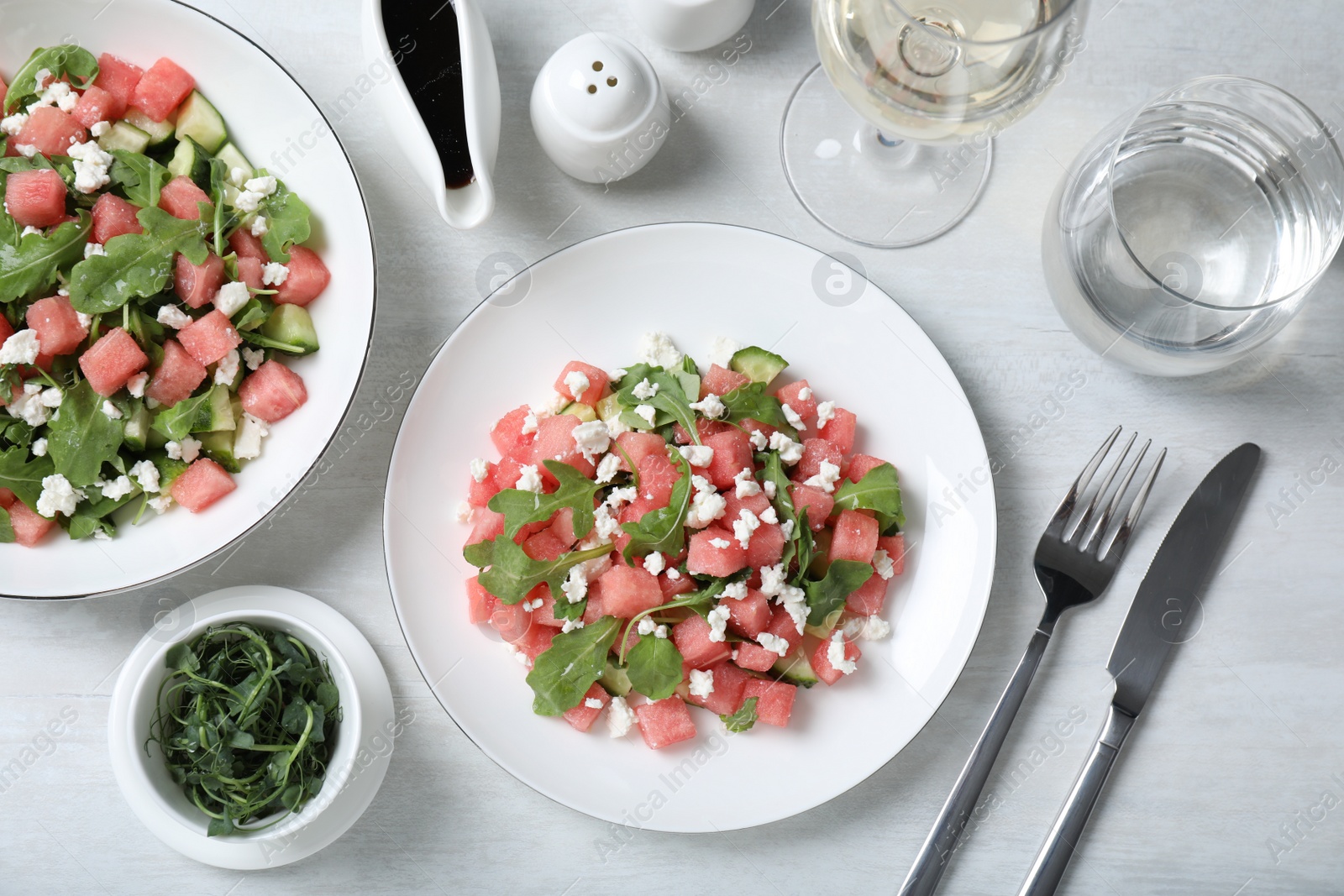 Photo of Delicious salad with watermelon, cucumber, arugula and feta cheese served on white wooden table, flat lay