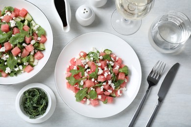 Photo of Delicious salad with watermelon, cucumber, arugula and feta cheese served on white wooden table, flat lay