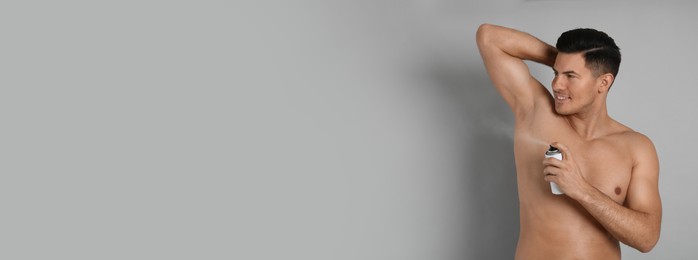Image of Handsome man applying deodorant to armpit on grey background, space for text. Banner design