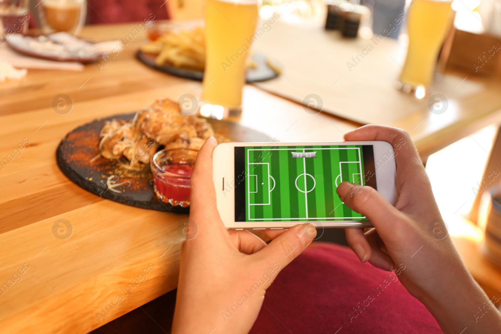 Photo of Woman playing game using smartphone at table with tasty BBQ wings in cafe, closeup