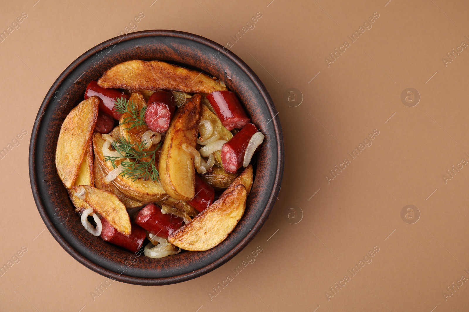 Photo of Delicious baked potato with thin dry smoked sausages, onion and dill in bowl on light brown table, top view. Space for text