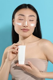 Photo of Beautiful young woman with sunscreen on her face holding sun protection cream against light blue background
