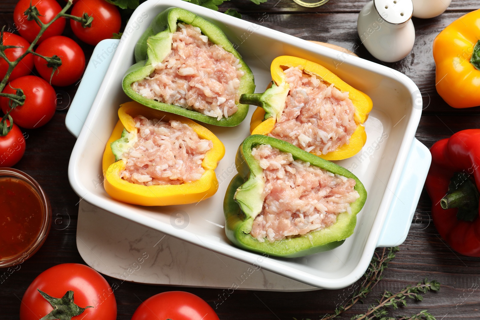Photo of Raw stuffed peppers in dish and ingredients on wooden table, flat lay