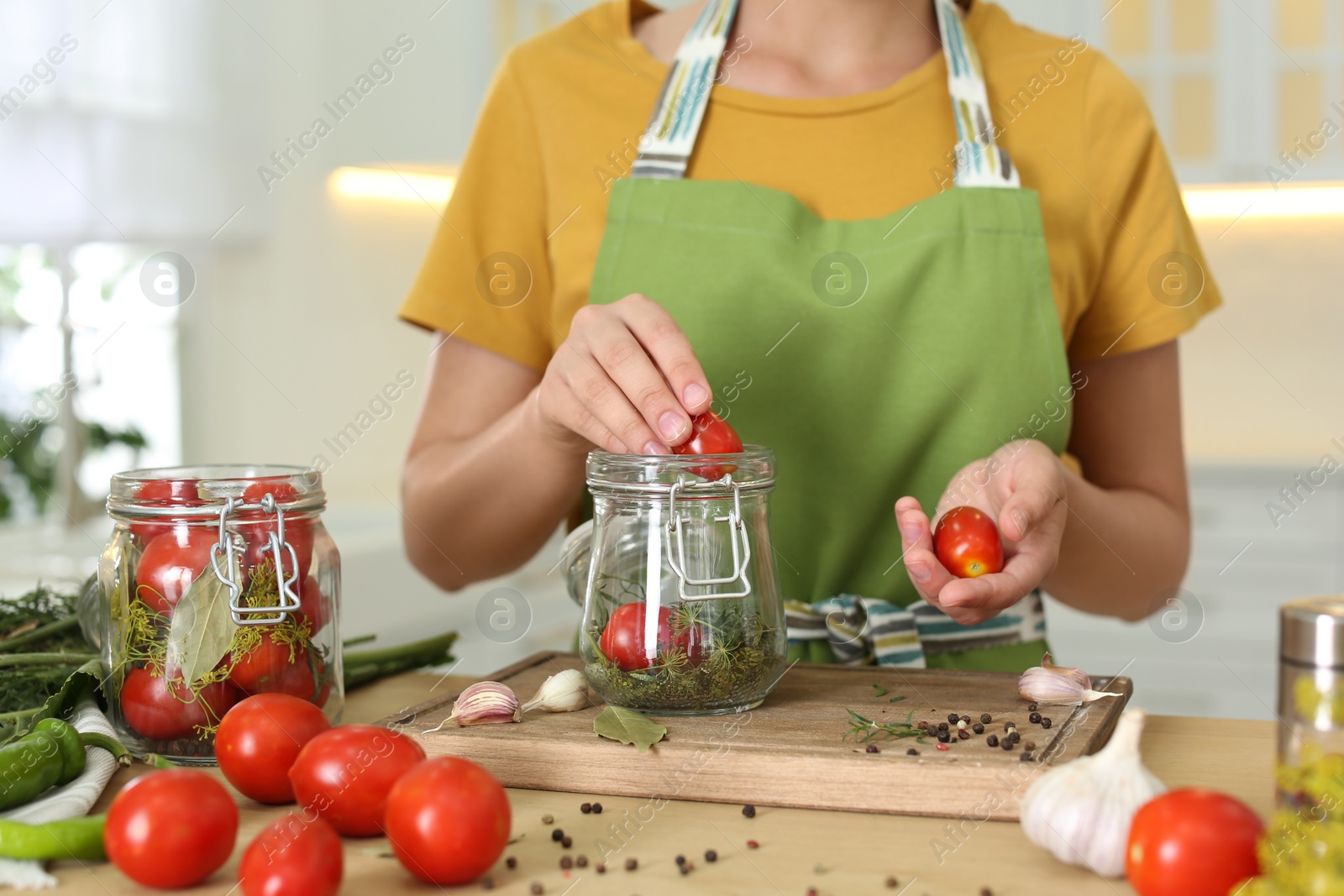 Photo of Woman putting tomatoes into pickling jar at table in kitchen, closeup