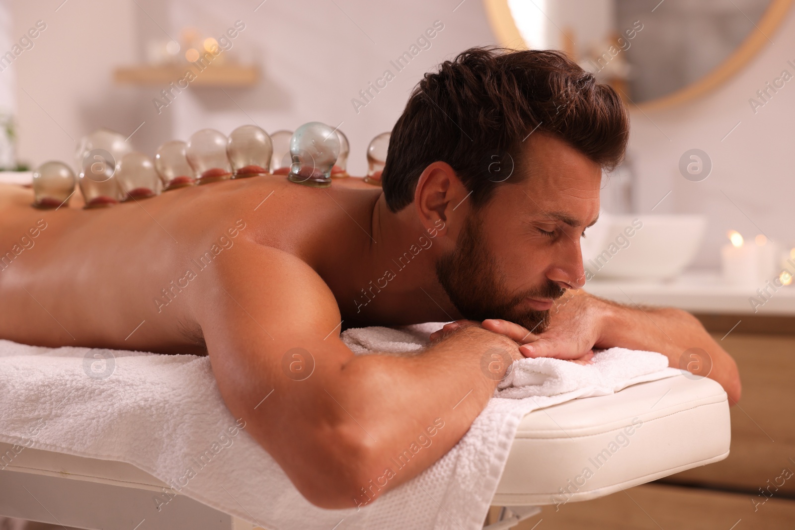 Photo of Cupping therapy. Man with glass cups on massage couch in spa salon