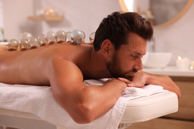 Photo of Cupping therapy. Man with glass cups on massage couch in spa salon