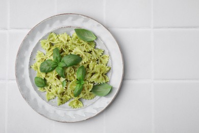 Photo of Delicious pasta with pesto sauce and basil on white tiled table, top view. Space for text