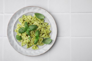 Delicious pasta with pesto sauce and basil on white tiled table, top view. Space for text