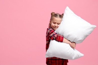 Photo of Girl in pajamas hugging pillow on pink background, space for text