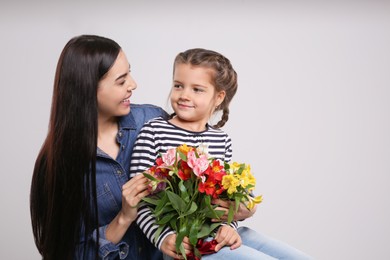 Photo of Happy woman with her cute daughter and bouquet of beautiful flowers on light grey background, space for text. Mother's day celebration