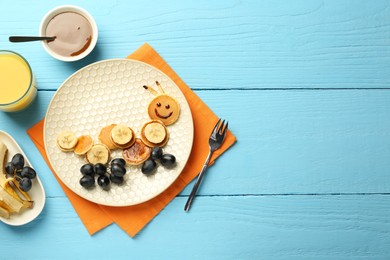 Photo of Creative serving for kids. Plate with cute caterpillar made of pancakes, grapes and banana on light blue wooden table, flat lay. Space for text