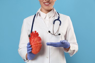 Doctor with stethoscope and model of heart on light blue background, closeup. Cardiology concept