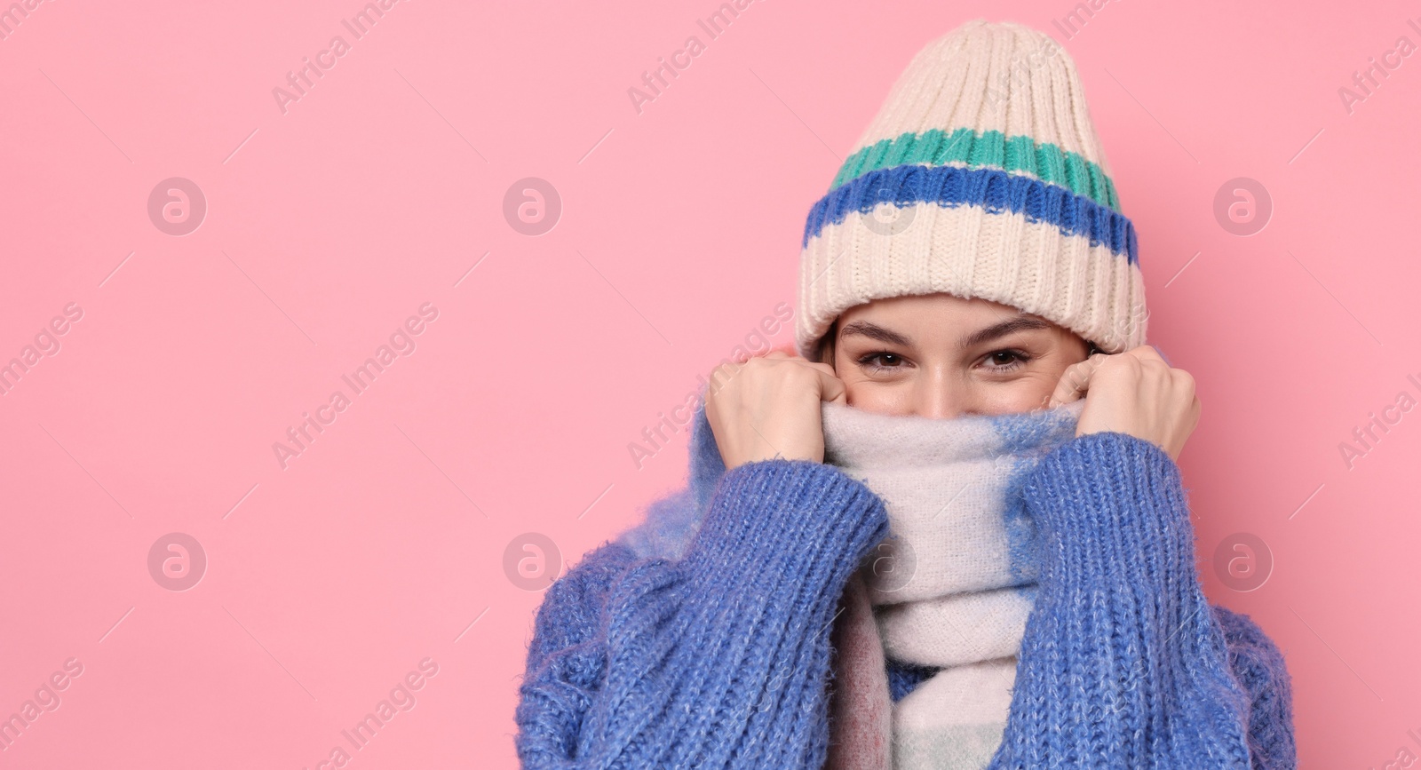 Photo of Beautiful woman in warm scarf and hat on pink background, space for text