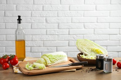 Photo of Cut fresh Chinese cabbage, tomatoes, oil and spices on wooden table near white brick wall