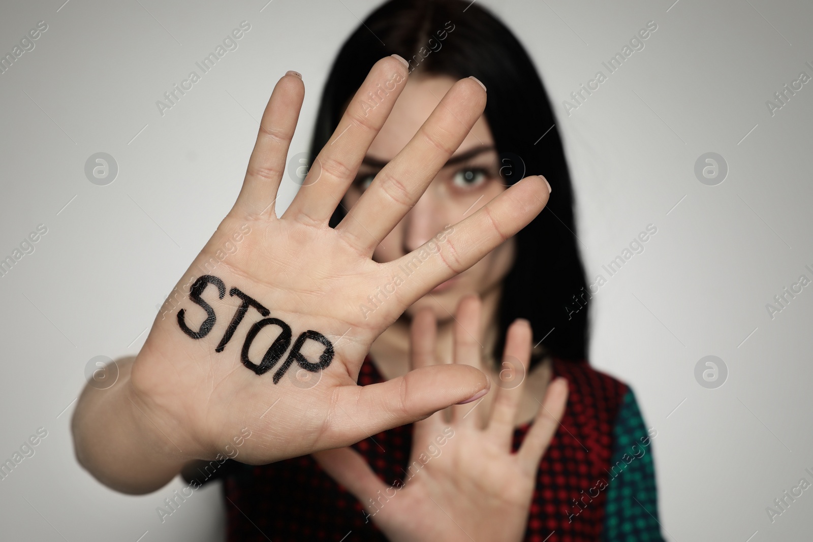 Photo of Young woman with word STOP written on her palm against light background, focus on hand