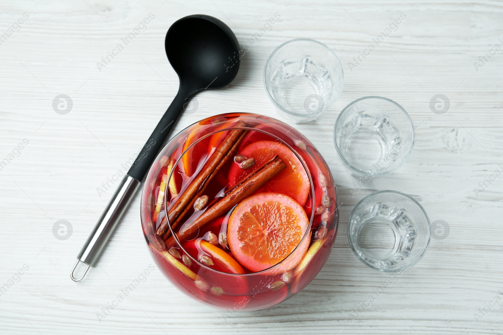 Photo of Empty glasses and ladle near bowl of aromatic punch drink on white wooden table, flat lay. Space for text