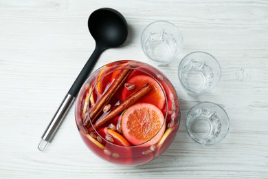 Photo of Empty glasses and ladle near bowl of aromatic punch drink on white wooden table, flat lay. Space for text