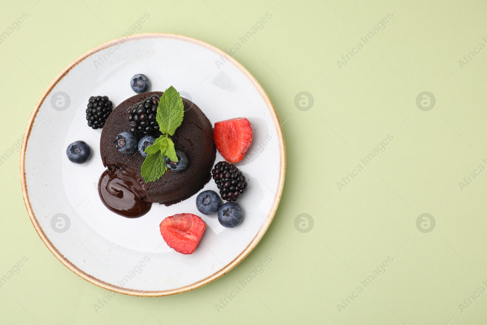 Photo of Plate with delicious chocolate fondant, berries and mint on light green table, top view. Space for text