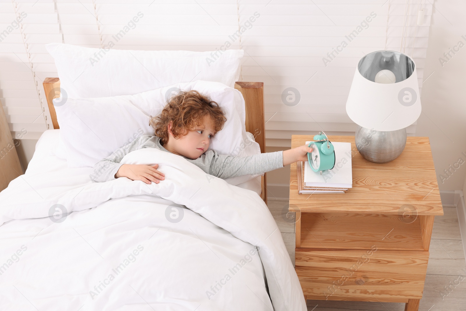 Photo of Little boy with alarm clock in bedroom