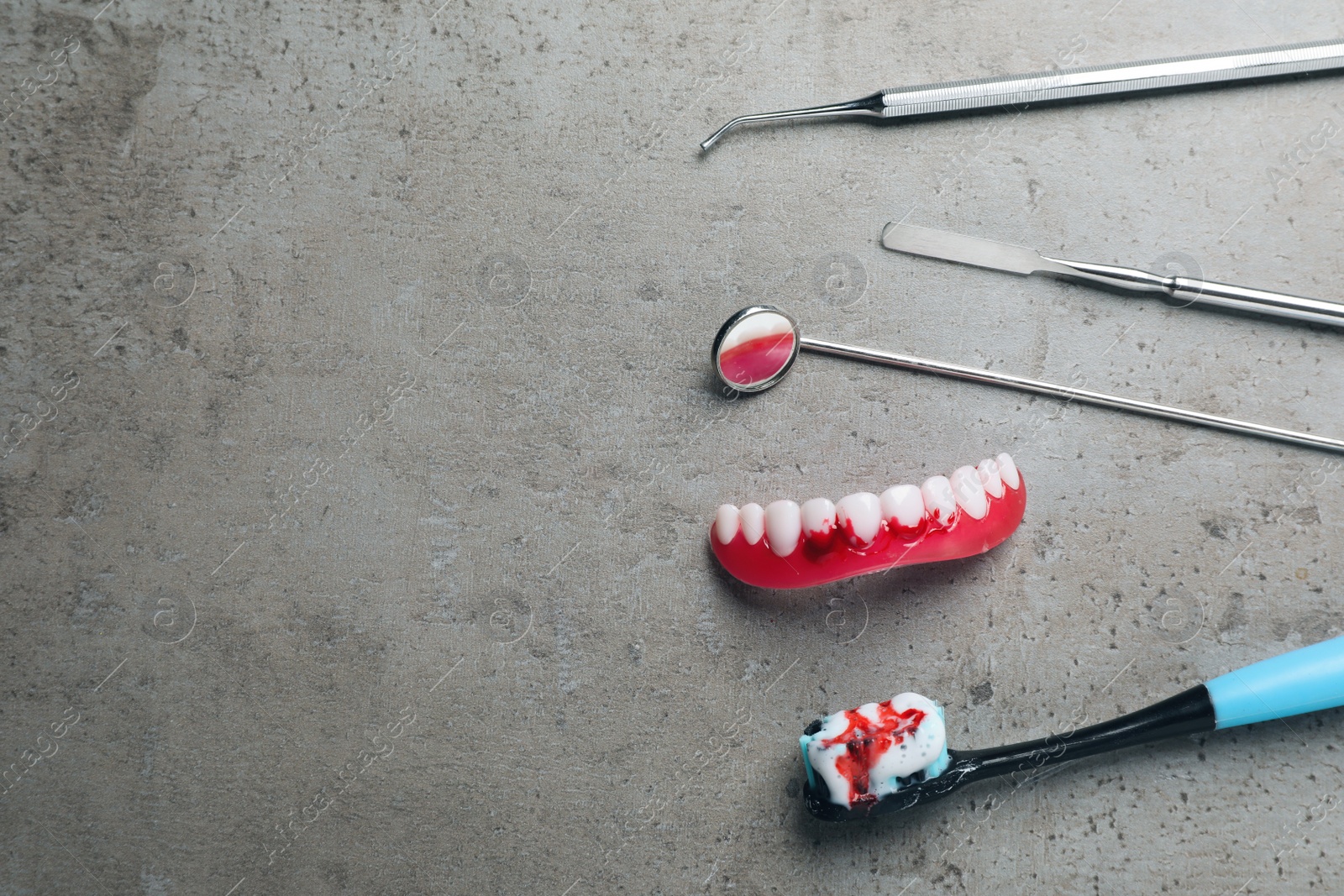 Photo of Dental instruments, gum model and toothbrush with blood on grey table, flat lay. Space for text