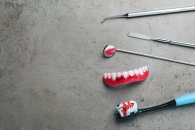 Dental instruments, gum model and toothbrush with blood on grey table, flat lay. Space for text
