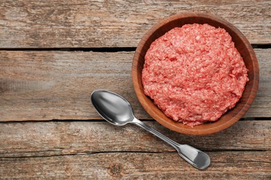 Photo of Bowl with raw fresh minced meat and spoon on wooden table, flat lay. Space for text