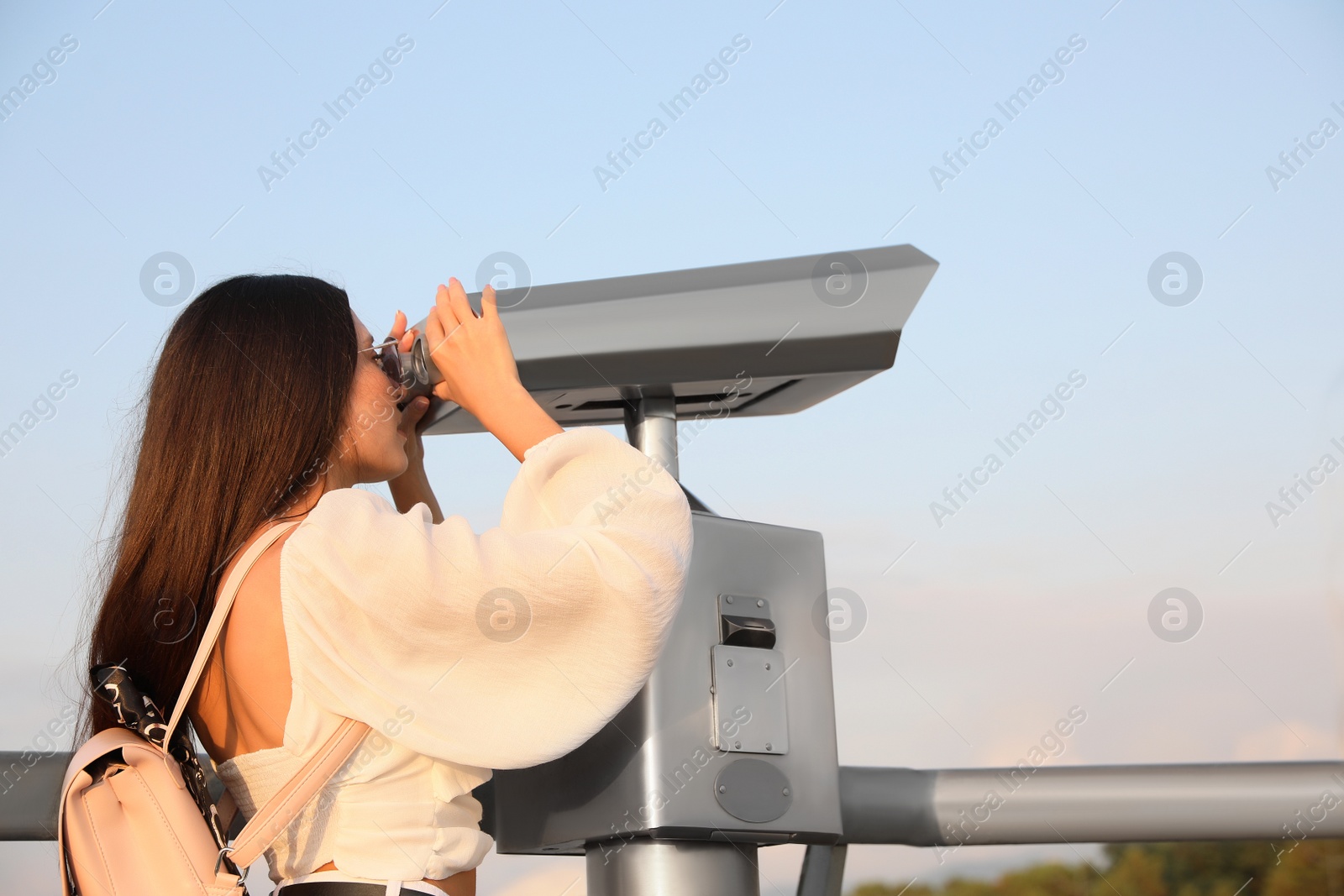 Photo of Young woman looking through tourist viewing machine at observation deck