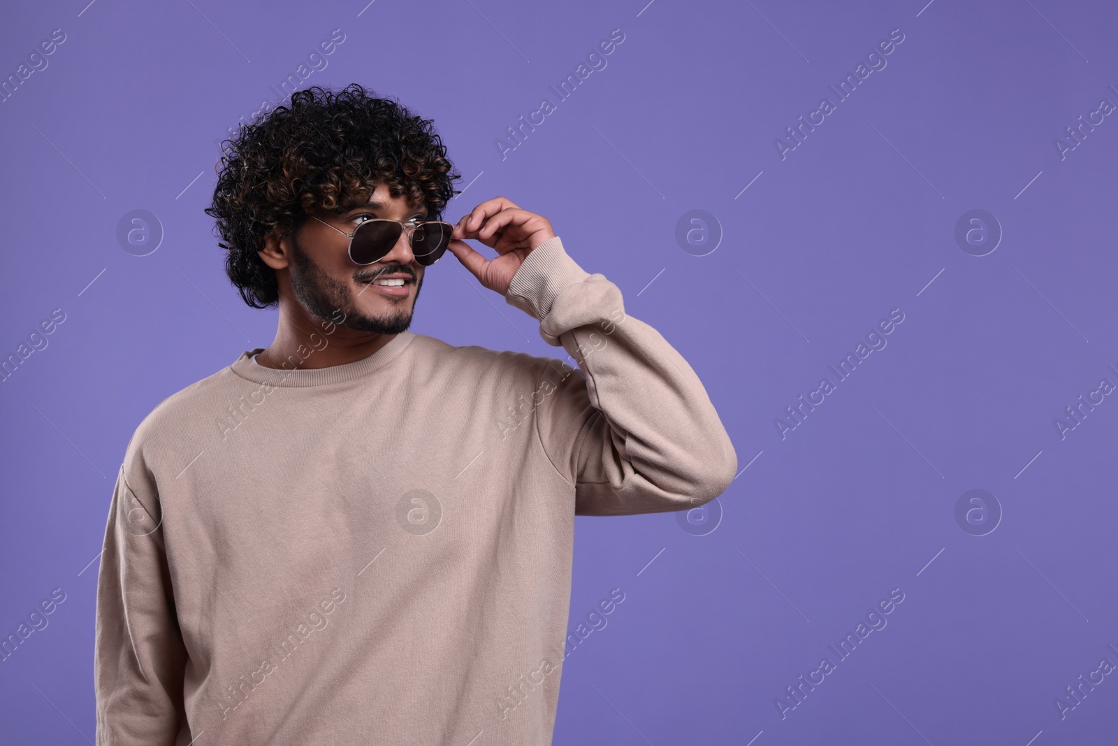 Photo of Handsome smiling man in sunglasses on violet background, space for text
