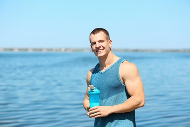 Athletic young man with protein shake at riverside