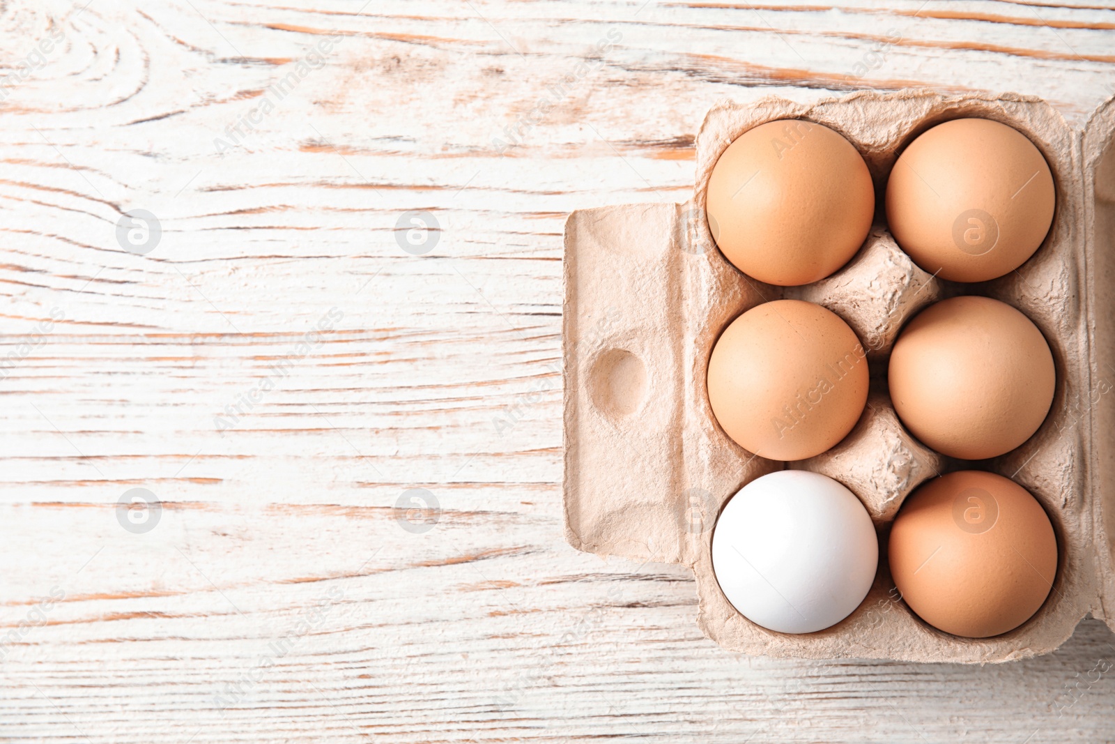 Photo of Carton of raw chicken eggs on wooden background, top view. Space for text