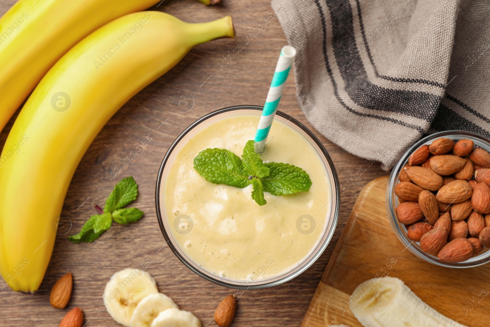 Photo of Flat lay composition of banana smoothie in glass and nuts on wooden table