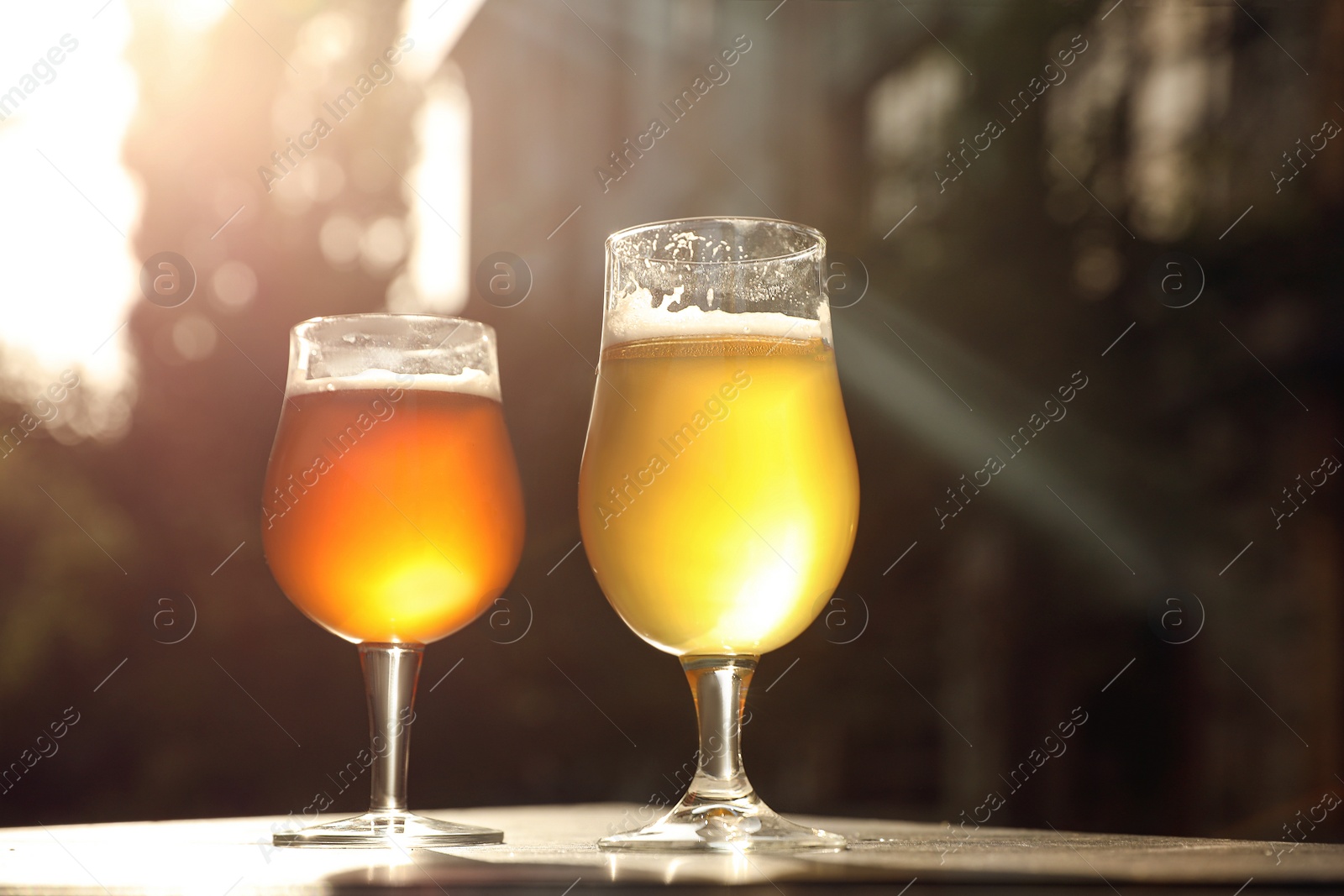 Photo of Glasses of cold tasty beer on wooden table outdoors