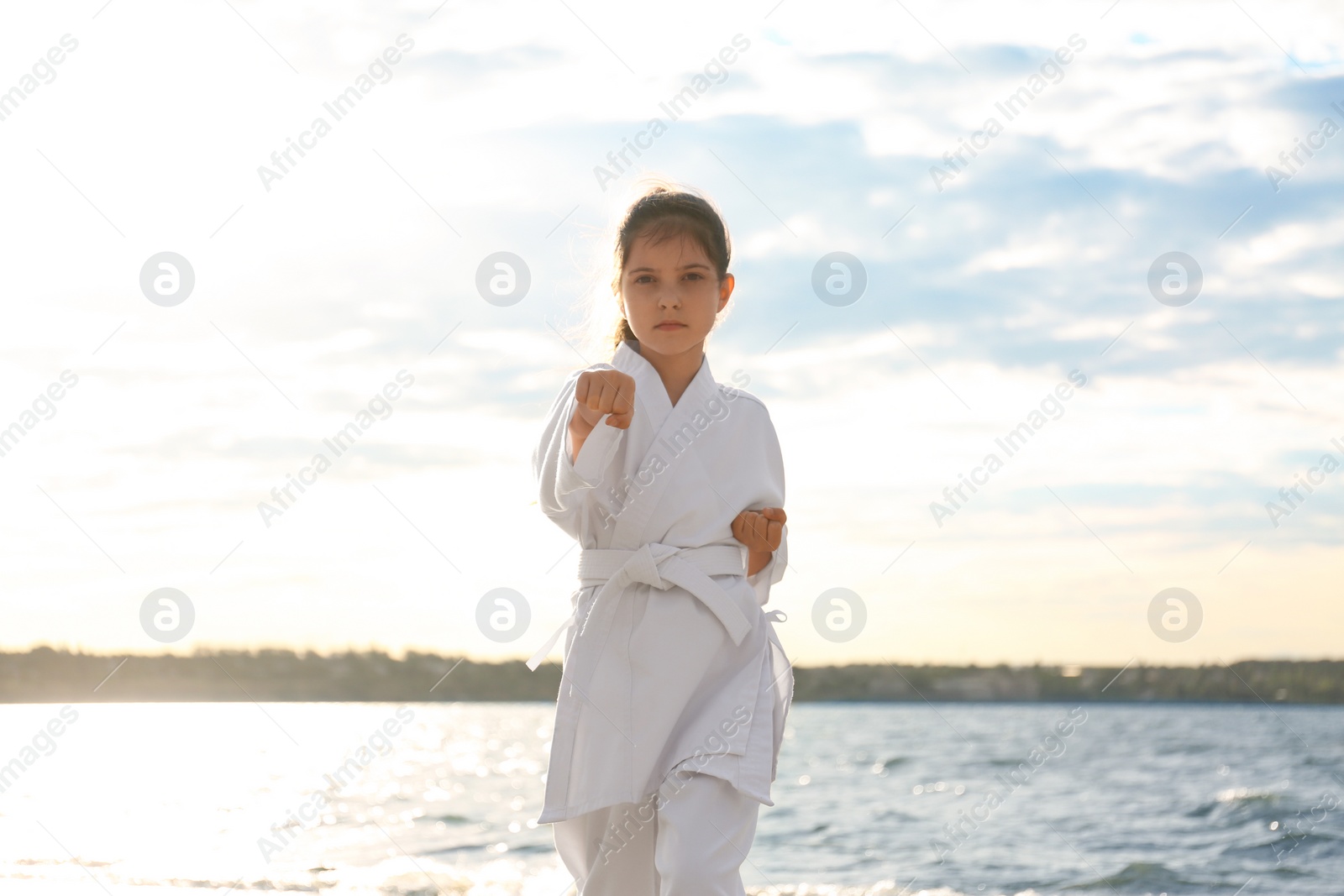 Photo of Cute little girl in kimono practicing karate near river