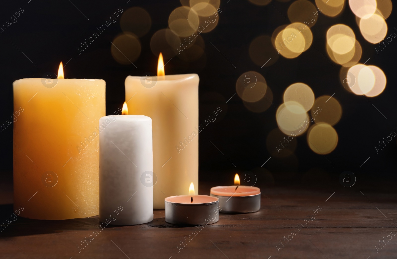 Image of Different wax candles burning on table against dark background with blurred lights. Bokeh effect