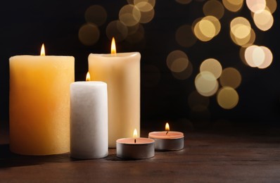 Image of Different wax candles burning on table against dark background with blurred lights. Bokeh effect